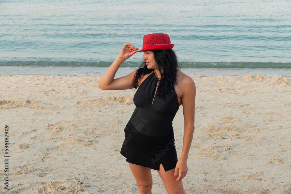 Gypsy girl in a red hat. Brunette in a black swimsuit on the beach.