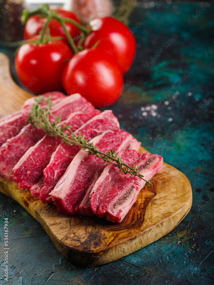 On a wooden cutting board, pieces of raw meat with a sprig of rosemary, appetizing ripe tomatoes on a turquoise marble background. Recipes for cooking homemade steaks.