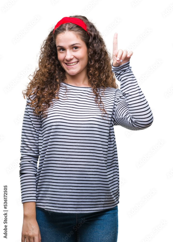Beautiful brunette curly hair young girl wearing stripes sweater over isolated background showing and pointing up with finger number one while smiling confident and happy. Beautiful brunette curly hair young girl wearing stripes sweater over isolated background showing and pointing up with finger number one while smiling confident and happy.