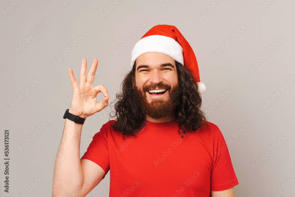 Confident bearded man wearing red Christmas hat is showing okay gesture. Confident bearded man wearing red Christmas hat is showing okay gesture.