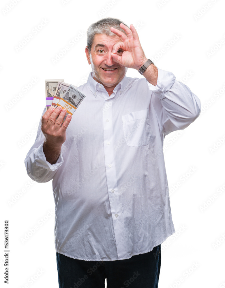 Handsome senior man holding bunch of money over isolated background with happy face smiling doing ok sign with hand on eye looking through fingers Handsome senior man holding bunch of money over isolated background with happy face smiling doing ok sign with hand on eye looking through fingers