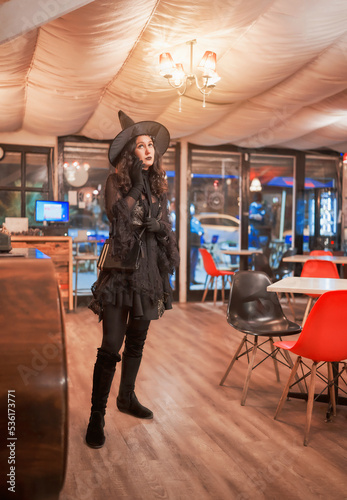 latin woman dressed as a witch in a cafe or restaurant standing and talking on the cell phone