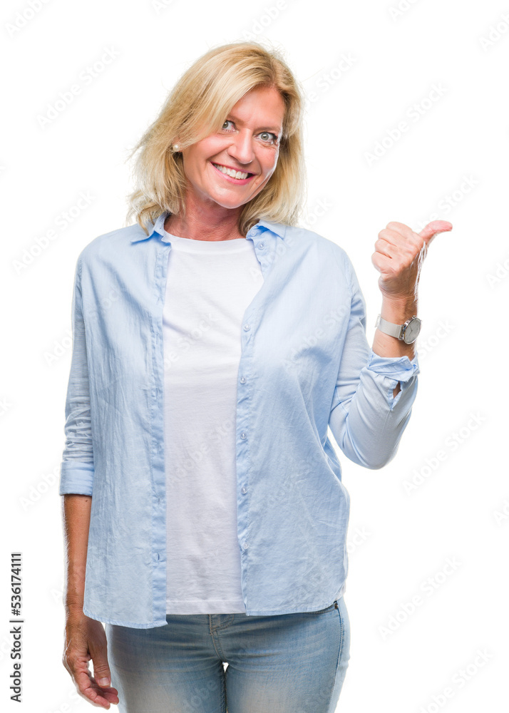 Middle age blonde woman over isolated background smiling with happy face looking and pointing to the side with thumb up. Middle age blonde woman over isolated background smiling with happy face looking and pointing to the side with thumb up.