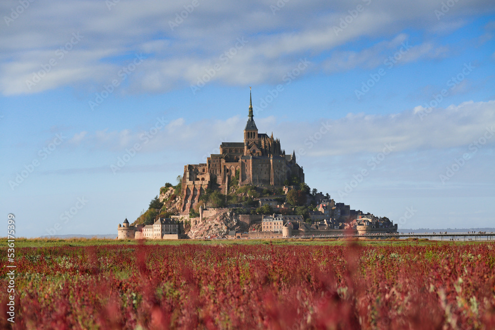 The Mont Saint-Michel fortress  tidal island with red and green grass and blue sky in background. Situated in France on the limit between Normandy and Brittany. 