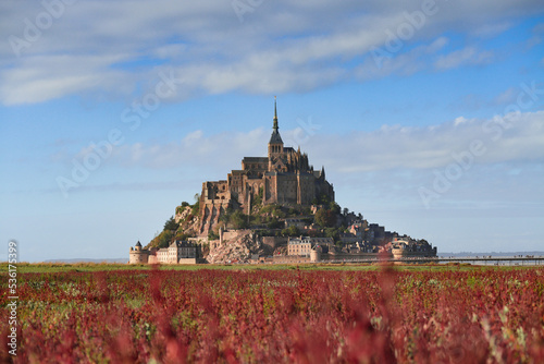 The Mont Saint-Michel fortress  tidal island with red and green grass and blue sky in background. Situated in France on the limit between Normandy and Brittany. 