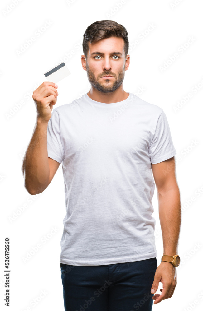 Young handsome man holding credit card over isolated background with a confident expression on smart face thinking serious