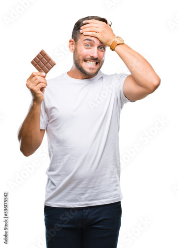 Young handsome man eating chocolate bar over isolated background stressed with hand on head, shocked with shame and surprise face, angry and frustrated. Fear and upset for mistake.