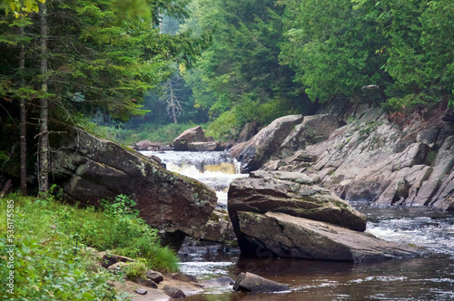 Misty  river waterfall flowing through large boulders in upstate new york, adirondack region, surrounded by large trees and dense forest.