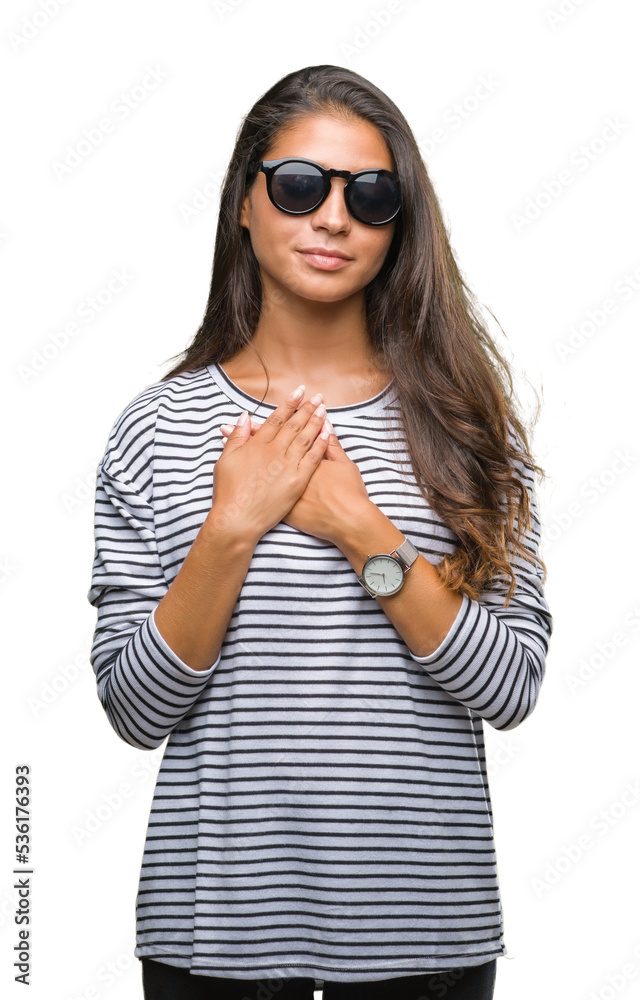 Young beautiful arab woman wearing sunglasses over isolated background smiling with hands on chest with closed eyes and grateful gesture on face. Health concept. Young beautiful arab woman wearing sunglasses over isolated background smiling with hands on chest with closed eyes and grateful gesture on face. Health concept.