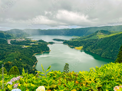 View from a high area of the lake at the foot of the mountains. Changeable weather in the Azores. Rain and sun