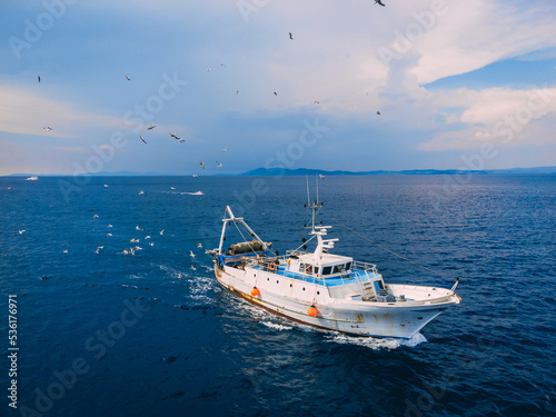 Top view of a fishing trawler coming back to the port and the seagulls following it.