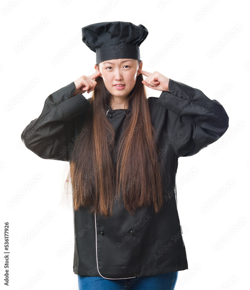 Young Chinese woman over isolated background wearing chef uniform covering ears with fingers with annoyed expression for the noise of loud music. Deaf concept. Young Chinese woman over isolated background wearing chef uniform covering ears with fingers with annoyed expression for the noise of loud music. Deaf concept.