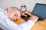 Person sleeps on the desk while working on laptop next to alarm clock