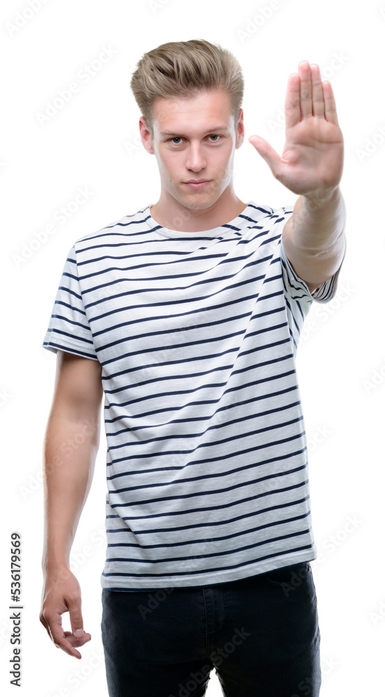 Young handsome blond man wearing stripes sailor t-shirt with open hand doing stop sign with serious and confident expression, defense gesture Young handsome blond man wearing stripes sailor t-shirt with open hand doing stop sign with serious and confident expression, defense gesture