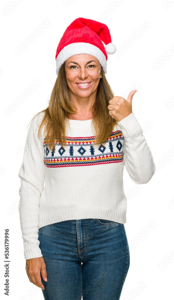 Middle age adult woman wearing winter sweater and chrismat hat over isolated background doing happy thumbs up gesture with hand. Approving expression looking at the camera with showing success. Middle age adult woman wearing winter sweater and chrismat hat over isolated background doing happy thumbs up gesture with hand. Approving expression looking at the camera with showing success.