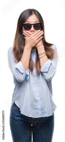 Young asian woman wearing sunglasses over isolated background shocked covering mouth with hands for mistake. Secret concept.