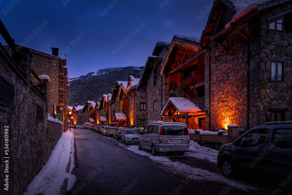 Modern stone houses and apartments illuminated by street lights in El Tarter village at dusk or night fall in Pyrenees mountains, Grandvalira, Andorra