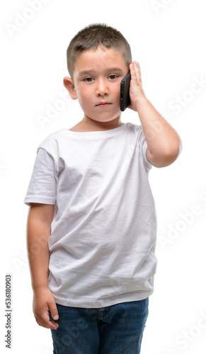 Dark haired little child using a smartphone with a confident expression on smart face thinking serious