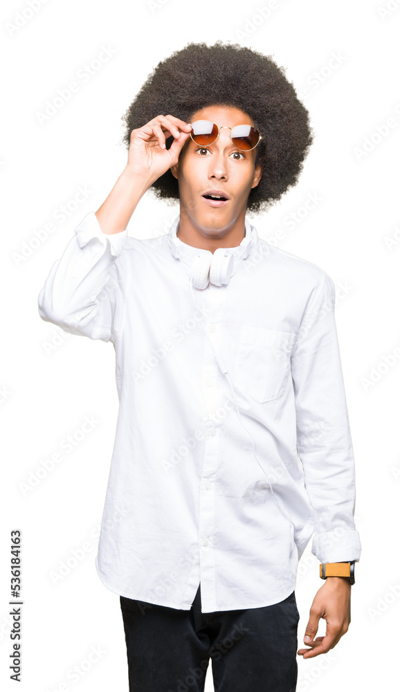 Young african american man with afro hair wearing sunglasses and headphones afraid and shocked with surprise expression, fear and excited face. Young african american man with afro hair wearing sunglasses and headphones afraid and shocked with surprise expression, fear and excited face.