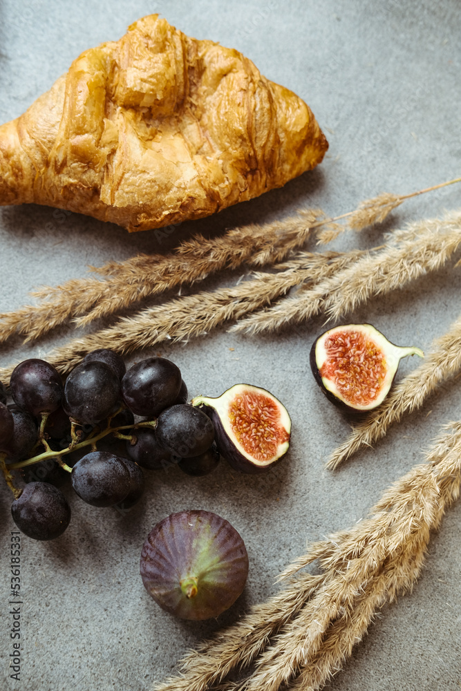 Autumn attributes. Croissant, dark grapes and figs on the grey table. Gold October Autumn attributes. Croissant, dark grapes and figs on the grey table. Gold October