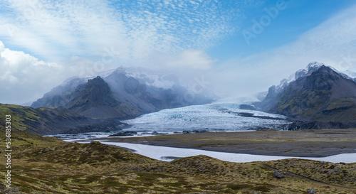 Glacier tongue slides from the Vatnajokull icecap or Vatna Glacier near subglacial Oraefajokull volcano, Iceland. Glacial lagoon with ice blocks and surrounding mountains. photo