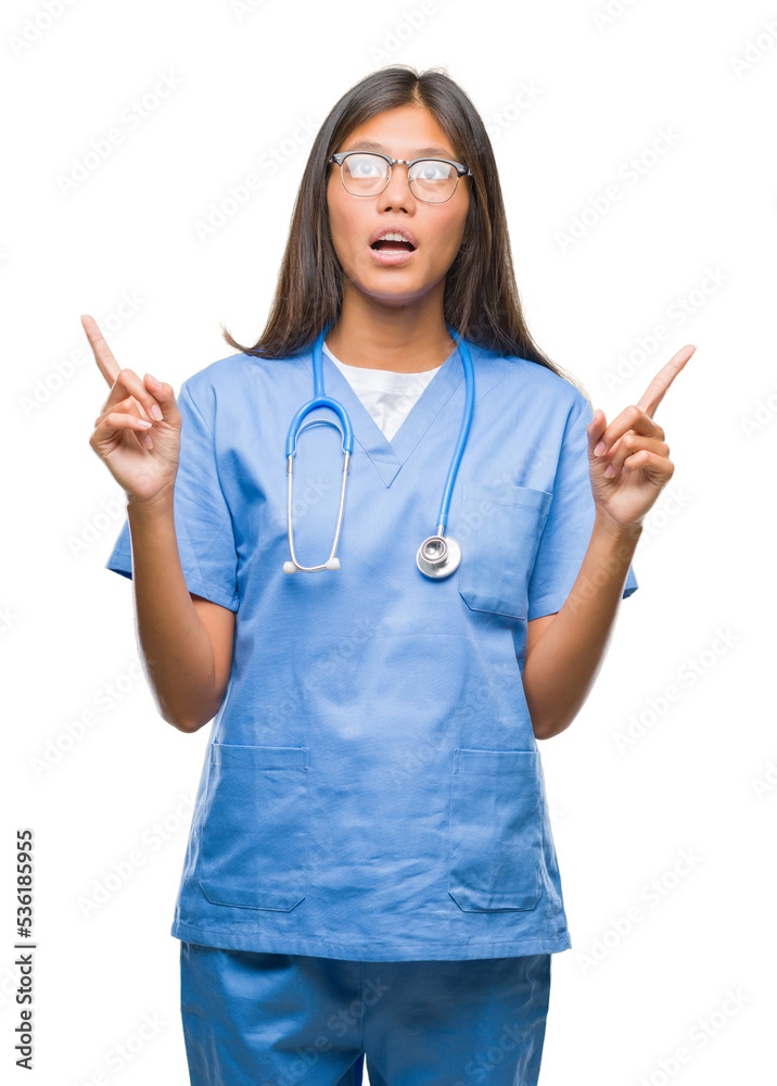 Young asian doctor woman over isolated background amazed and surprised looking up and pointing with fingers and raised arms. Young asian doctor woman over isolated background amazed and surprised looking up and pointing with fingers and raised arms.