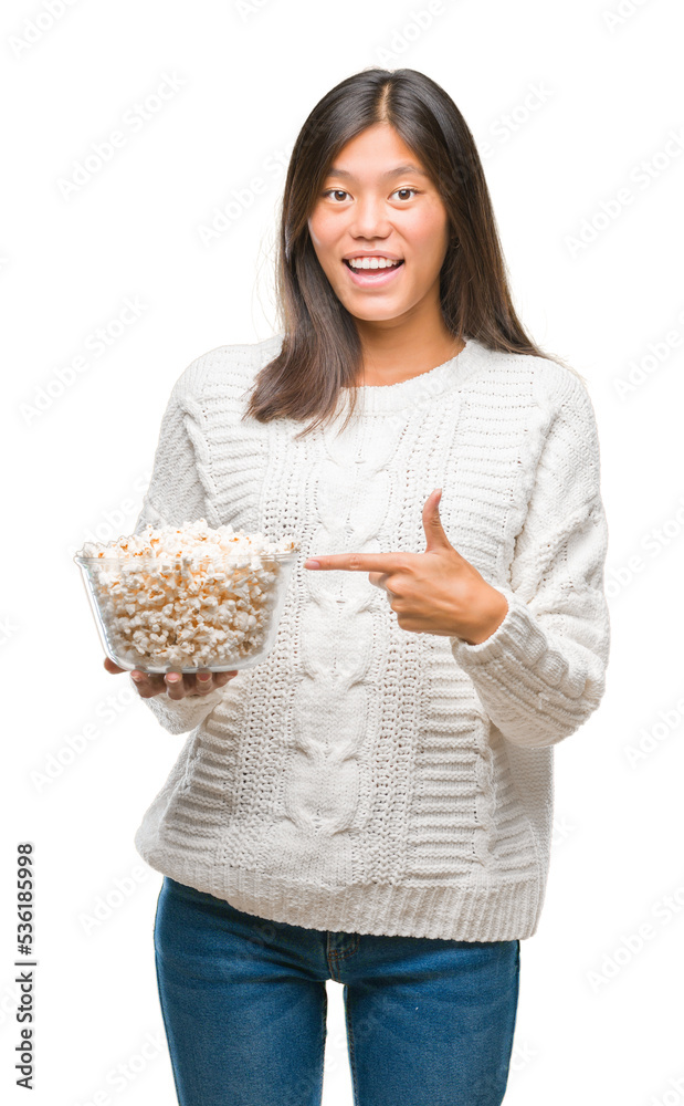 Young asian woman eating popcorn over isolated background very happy pointing with hand and finger Young asian woman eating popcorn over isolated background very happy pointing with hand and finger