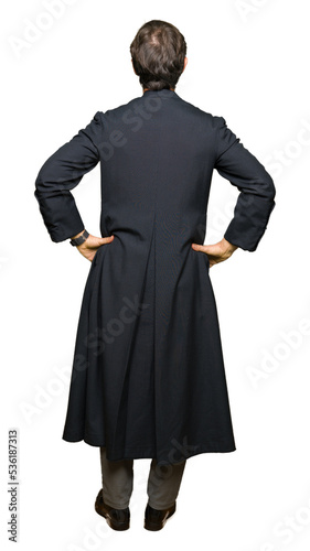 Middle age priest man wearing catholic robe standing backwards looking away with arms on body