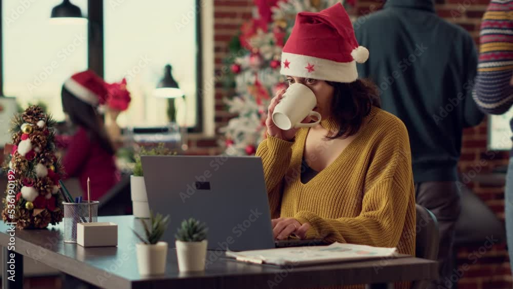 Office worker planning startup project on laptop during winter season festivity, using computer at desk. Festive woman working in space with seasonal decorations and christmas tree.