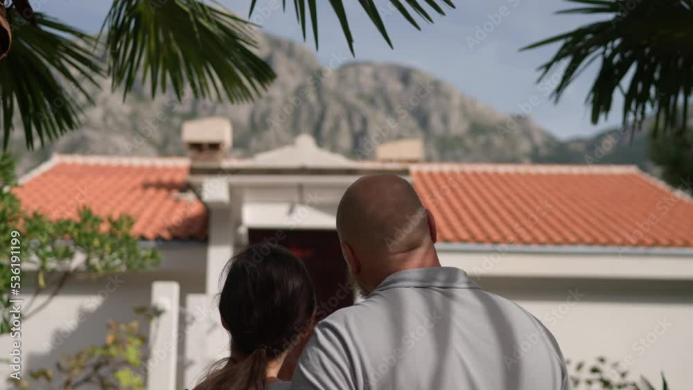 Rear on Asian American young just-married couple standing at yard of house, hugging and observing second floor. Back view on man and woman in hugs moving in new home. Rear on Asian American young just-married couple standing at yard of house, hugging and observing second floor. Back view on man and woman in hugs moving in new home.