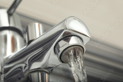 Water flowing from bath tap on blurred background, closeup