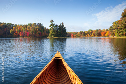 Wooden canoe moves on a blue lake with trees in autumn color and a small island in northern Minnesota photo
