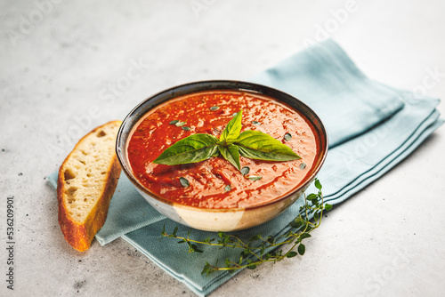 Bowl of fresh homemade tomato basil soup with fresh herbs and slice of focaccia bread on a blue napkin photo