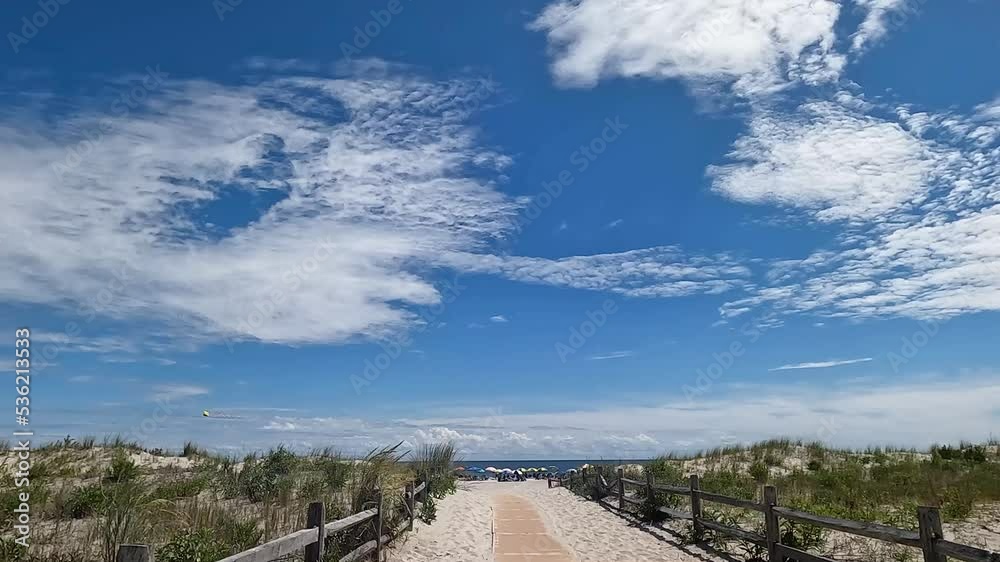 View of beach entrance surrounded by American beach grass dunes. Donut shaped cloud in a blue sky over the beach. View of beach entrance surrounded by American beach grass dunes. Donut shaped cloud in a blue sky over the beach.