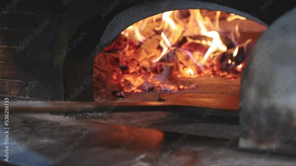 Fresh traditional rustical pizza with salami, green peperoni, cheese and tomatoe souce get shoved into oven fired by wood with beutiful flames