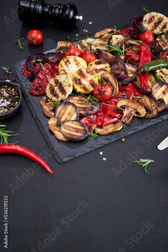 Grilled vegetables mix on a stone serving board - zucchini eggplant onions corn mushroom tomato