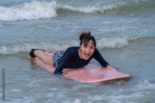 Tourist Asian woman wearing sportswear to practice surfboarding lies on a surfing serif at the beach on vacation. water sports and adventure concept © Supavadee
