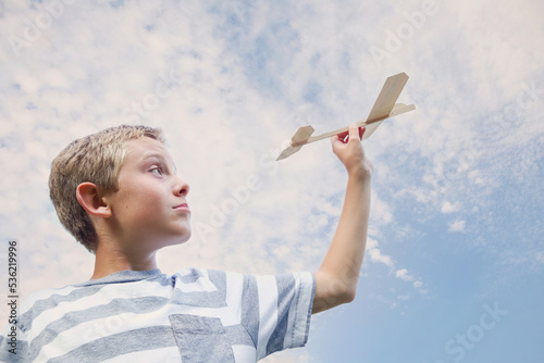Boy flying a toy Balsa wood airplane in a cloudy sky