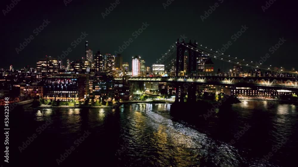 aerial over East River water towards Brooklyn along Manhattan Bridge at night in New York City NYC aerial over East River water towards Brooklyn along Manhattan Bridge at night in New York City NYC