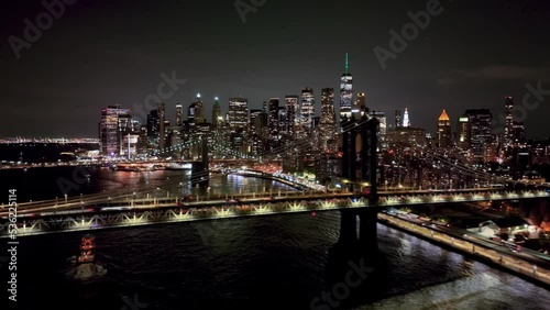 aerial view of cars driving across over Manhattan Bridge and Brooklyn Bridges on East River with Freedom Tower and skyline bright lights in New York City at night in NYC