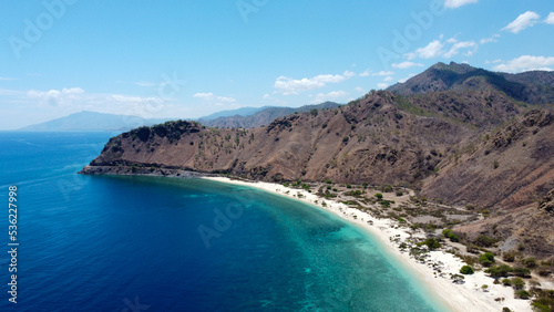 Aerial drone view of beautiful white sandy beach with green and blue ocean water and dry mountainous landscape in Dili, Timor Leste, Southeast Asia