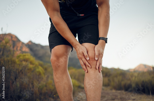 Man, knee pain and injury in fitness exercise, training and health workout in nature park or countryside hiking trail. Zoom, hands and sports runner with risk emergency and medical leg accident photo