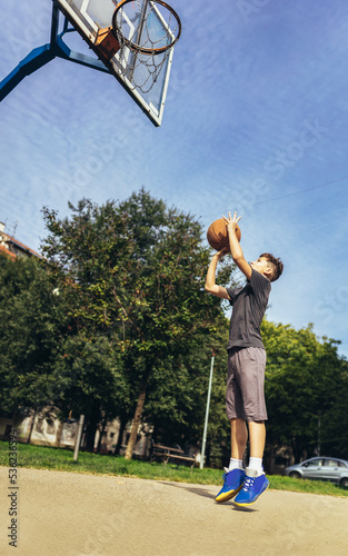 Cute boy in gray t shirt plays basketball on city playground. © Mediteraneo