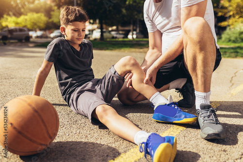 Fotografie Father helping boy with knee trauma after playing basketball