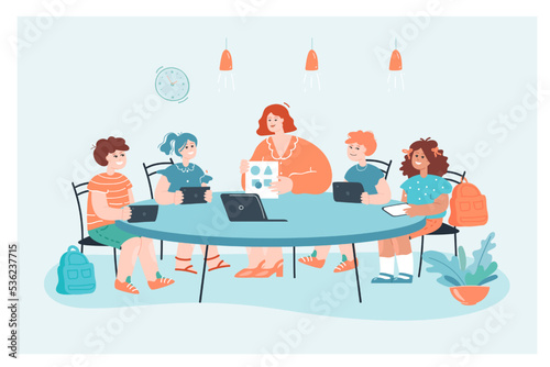 Teacher cartoon character showing picture to group of children. Woman sitting at table in circle with girls and boys holding tablets in classroom flat vector illustration. Education, school concept