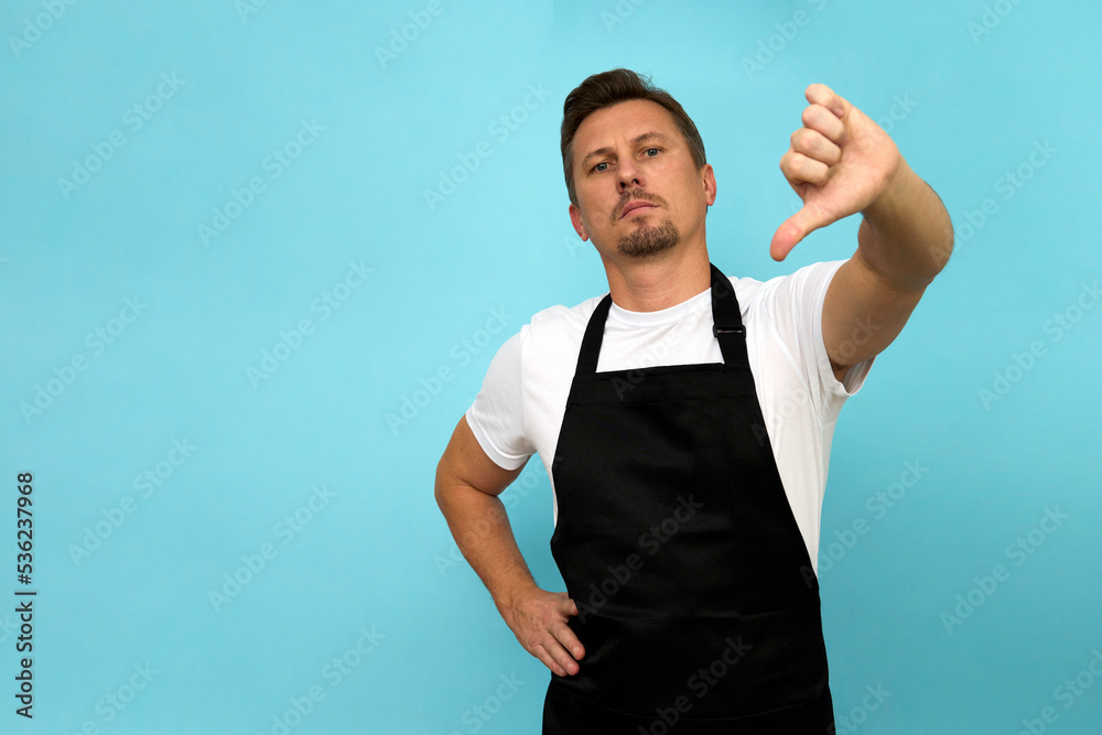 Young barista in black apron and white t-shirt on blue background Young barista in black apron and white t-shirt on blue background