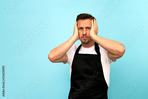 Young barista in black apron and white t-shirt on blue background