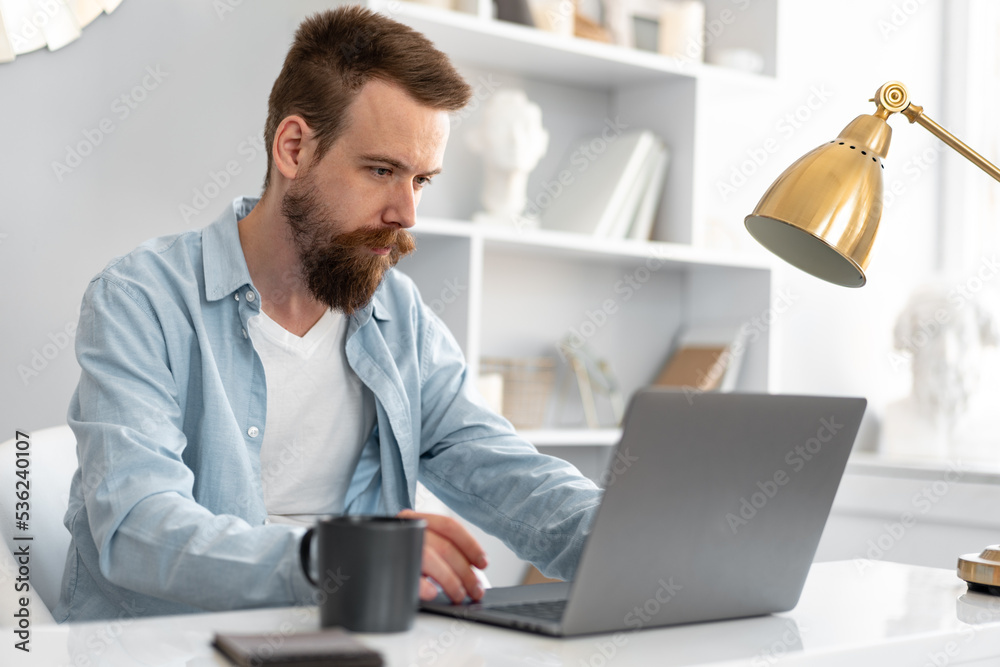 Stylish bearded man working on laptop from home sitting at the table Stylish bearded man working on laptop from home sitting at the table