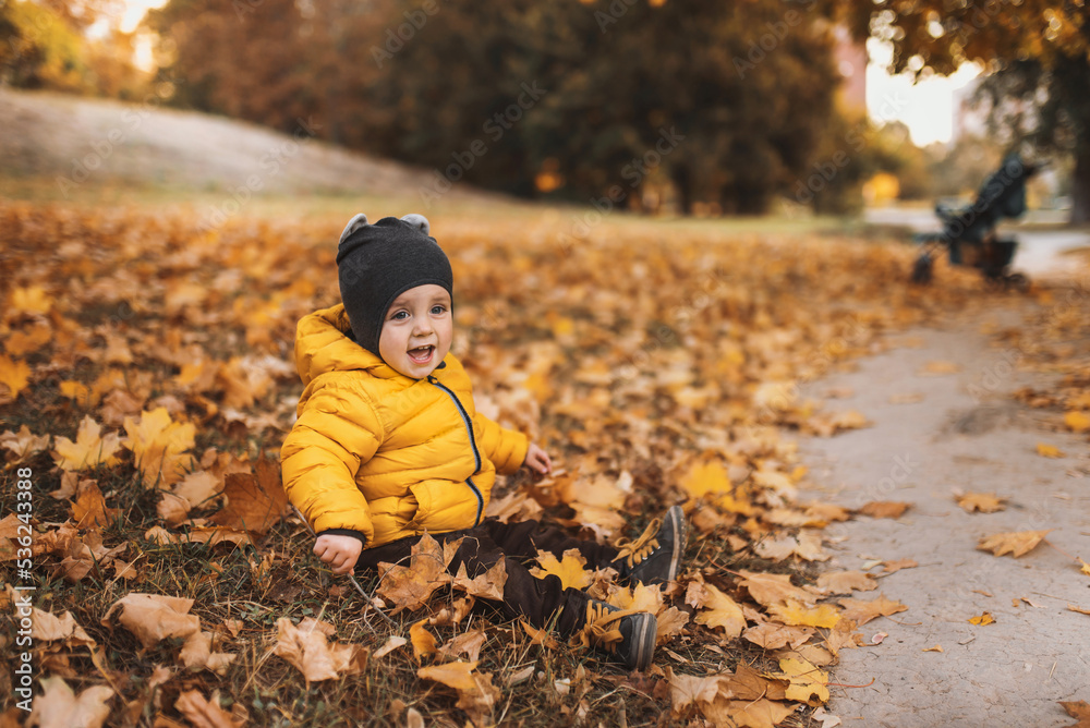 Little boy in yellow jacket playing with autumn fallen leaves in park. Child laughing throwing up orange maple leaves. Little boy in yellow jacket playing with autumn fallen leaves in park. Child laughing throwing up orange maple leaves.