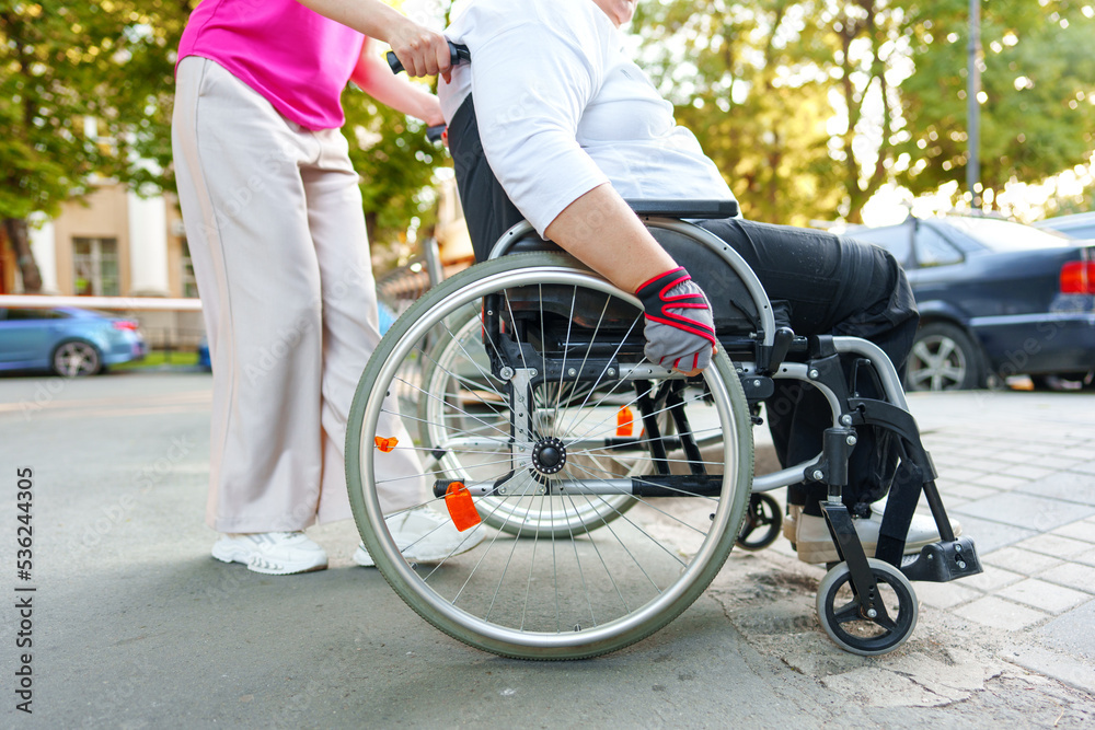 Obraz premium Young female caregiver pushing wheelchair with female person with disability across city street